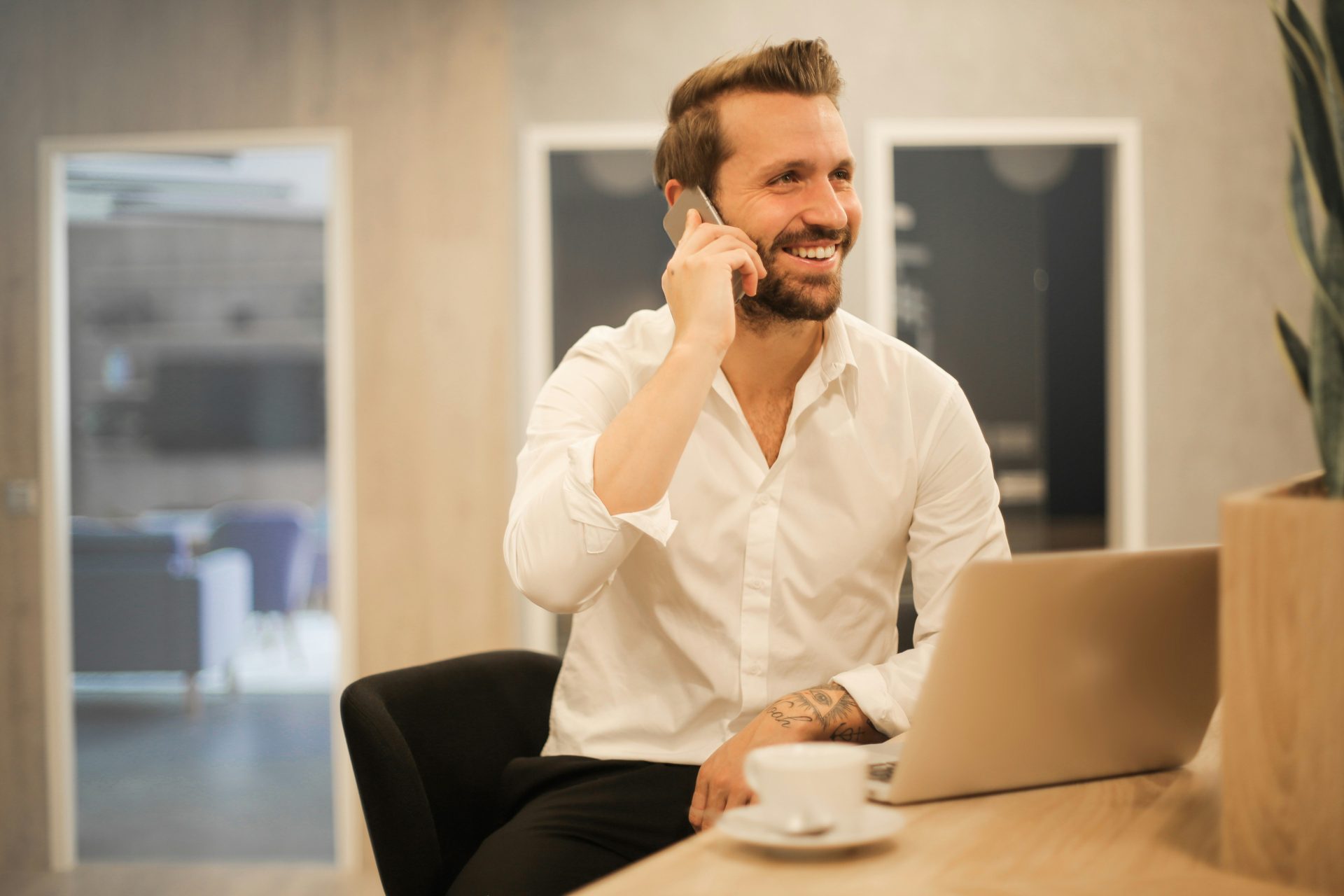 Man smiling on phone beside laptop.