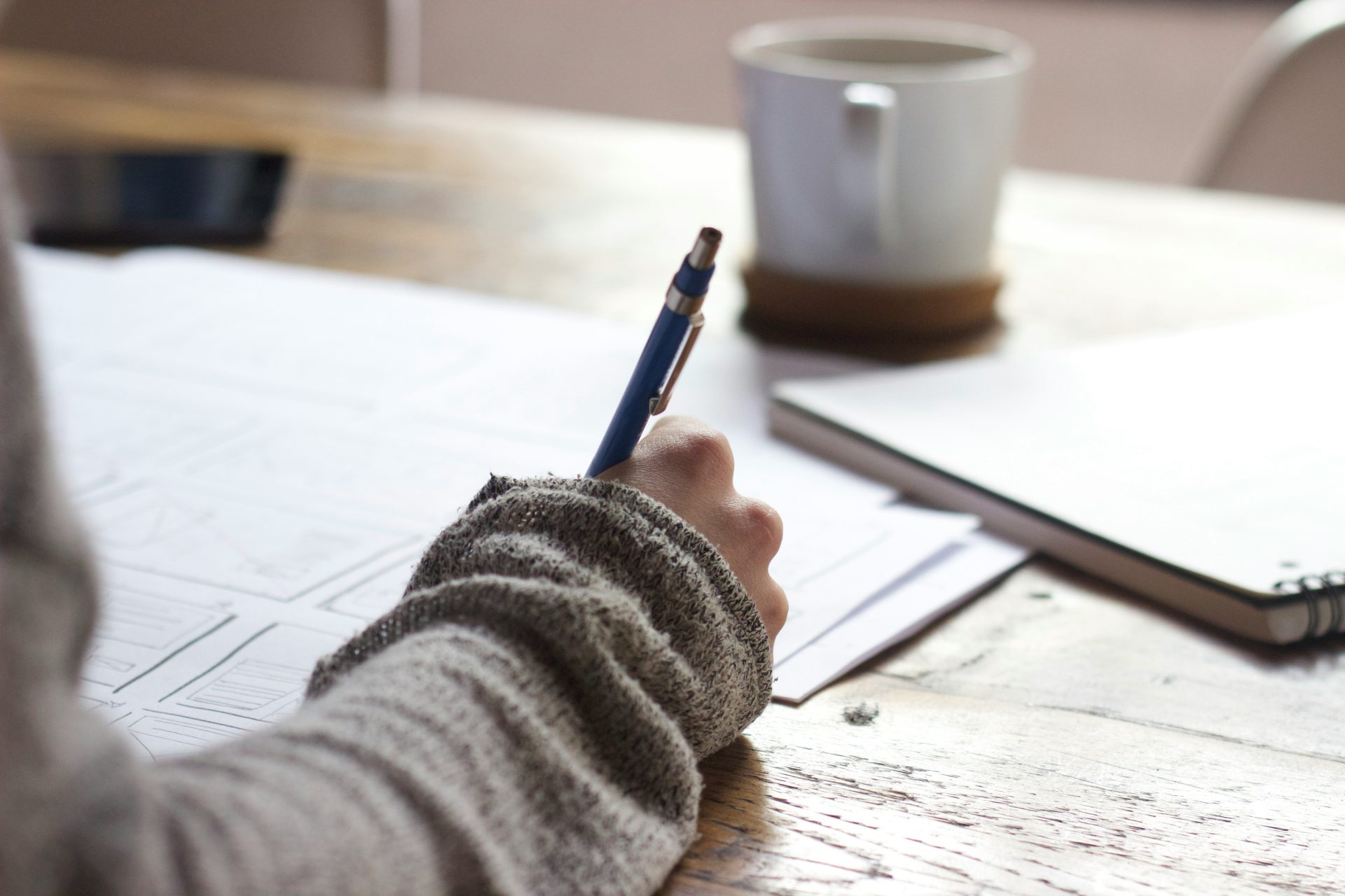 Handwriting on paper next to coffee cup.